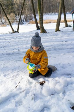 Child having fun in the snow, wearing winter clothing in snowy landscape during daytime. Child with a big smile surrounded by snowy trees and a clear blue sky.