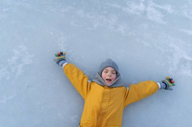 Child having fun in the snow, wearing winter clothing in snowy landscape during daytime. Child with a big smile surrounded by snowy trees and a clear blue sky.