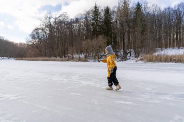 Child having fun in the snow, wearing winter clothing in snowy landscape during daytime. Child with a big smile surrounded by snowy trees and a clear blue sky.