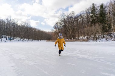 Child having fun in the snow, wearing winter clothing in snowy landscape during daytime. Child with a big smile surrounded by snowy trees and a clear blue sky.