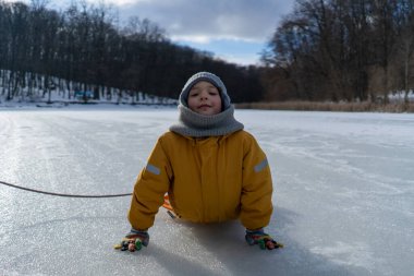 Child having fun in the snow, wearing winter clothing in snowy landscape during daytime. Child with a big smile surrounded by snowy trees and a clear blue sky.