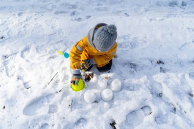 Child having fun in the snow, wearing winter clothing in snowy landscape during daytime. Child with a big smile surrounded by snowy trees and a clear blue sky.