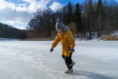 Child having fun in the snow, wearing winter clothing in snowy landscape during daytime. Child with a big smile surrounded by snowy trees and a clear blue sky.