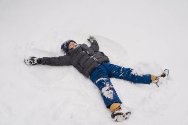 Mutlu çocuk dışarıda kışın tadını çıkarıyor. Sıcak kışlık giysiler ve örgü şapka giyen, soğuk bir kar gününde karda oynayan gülümseyen çocuk. Doğal ışık yaşam tarzı portresi ve çocukluk mutluluğu.