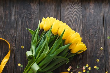 Sarı kurdeleli bir buket sarı lale, ahşap bir arka planda yatıyor. Baharın sembolü. 8 Mart, Anneler Günü, Paskalya veya bahar promosyonları için bayram kartları, selamlar, tasarım için ideal.