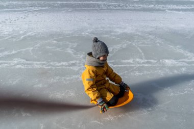 Child having fun in the snow, wearing winter clothing in snowy landscape during daytime. Child with a big smile surrounded by snowy trees and a clear blue sky.