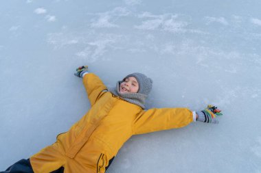 Child having fun in the snow, wearing winter clothing in snowy landscape during daytime. Child with a big smile surrounded by snowy trees and a clear blue sky.