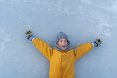 Child having fun in the snow, wearing winter clothing in snowy landscape during daytime. Child with a big smile surrounded by snowy trees and a clear blue sky.