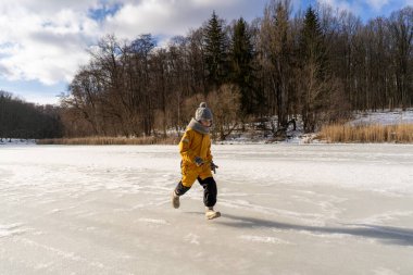 Child having fun in the snow, wearing winter clothing in snowy landscape during daytime. Child with a big smile surrounded by snowy trees and a clear blue sky.
