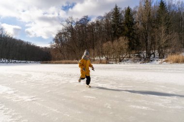 Child having fun in the snow, wearing winter clothing in snowy landscape during daytime. Child with a big smile surrounded by snowy trees and a clear blue sky.