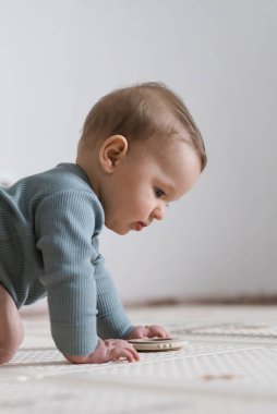 Yumuşak bir oyun hasırının üzerinde karnının üzerine uzanmış duyusal bir oyuncakla oynayan sevimli bir bebek. Bebek, oyuncağı keşfederken odaklanmış ve meraklı, erken öğrenme ve motor beceri geliştirmeyi destekliyor.