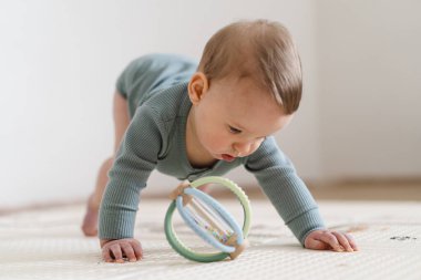 Yumuşak bir oyun hasırının üzerinde karnının üzerine uzanmış duyusal bir oyuncakla oynayan sevimli bir bebek. Bebek, oyuncağı keşfederken odaklanmış ve meraklı, erken öğrenme ve motor beceri geliştirmeyi destekliyor.