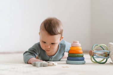 Yumuşak bir oyun hasırının üzerinde karnının üzerine uzanmış duyusal bir oyuncakla oynayan sevimli bir bebek. Bebek, oyuncağı keşfederken odaklanmış ve meraklı, erken öğrenme ve motor beceri geliştirmeyi destekliyor.