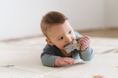 Yumuşak bir oyun hasırının üzerinde karnının üzerine uzanmış duyusal bir oyuncakla oynayan sevimli bir bebek. Bebek, oyuncağı keşfederken odaklanmış ve meraklı, erken öğrenme ve motor beceri geliştirmeyi destekliyor.