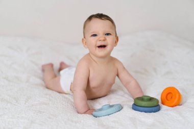 Yumuşak bir battaniyenin üzerinde göbeğin üzerine uzanmış sevimli bir bebek ve renkli bir yüzük oyuncağıyla oynuyor. Erken çocukluk gelişimi, ebeveynlik bakımı, mutlu aile anları ve bebek yaşam tarzı kavramı.