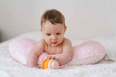 Bebek yumuşak bir yastığa uzanır, renkli bir oyuncağa uzanır. Erken çocukluk gelişimi, ebeveynlik bakımı, mutlu aile anları ve bebek yaşam tarzı kavramı.