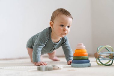 Yumuşak bir oyun hasırının üzerinde karnının üzerine uzanmış duyusal bir oyuncakla oynayan sevimli bir bebek. Bebek, oyuncağı keşfederken odaklanmış ve meraklı, erken öğrenme ve motor beceri geliştirmeyi destekliyor.