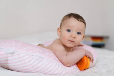 Bebek yumuşak bir yastığa uzanır, renkli bir oyuncağa uzanır. Erken çocukluk gelişimi, ebeveynlik bakımı, mutlu aile anları ve bebek yaşam tarzı kavramı.