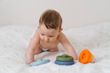 Yumuşak bir battaniyenin üzerinde göbeğin üzerine uzanmış sevimli bir bebek ve renkli bir yüzük oyuncağıyla oynuyor. Erken çocukluk gelişimi, ebeveynlik bakımı, mutlu aile anları ve bebek yaşam tarzı kavramı.