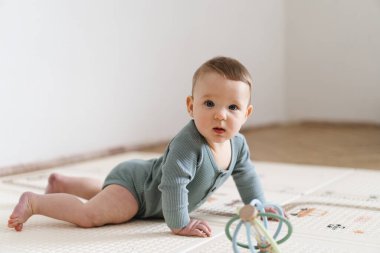 Yumuşak bir oyun hasırının üzerinde karnının üzerine uzanmış duyusal bir oyuncakla oynayan sevimli bir bebek. Bebek, oyuncağı keşfederken odaklanmış ve meraklı, erken öğrenme ve motor beceri geliştirmeyi destekliyor.