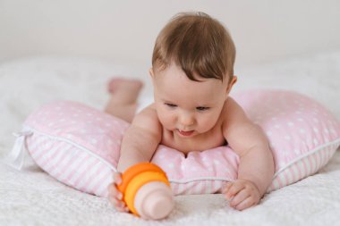 Bebek yumuşak bir yastığa uzanır, renkli bir oyuncağa uzanır. Erken çocukluk gelişimi, ebeveynlik bakımı, mutlu aile anları ve bebek yaşam tarzı kavramı.