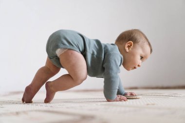 Yumuşak bir oyun hasırının üzerinde karnının üzerine uzanmış duyusal bir oyuncakla oynayan sevimli bir bebek. Bebek, oyuncağı keşfederken odaklanmış ve meraklı, erken öğrenme ve motor beceri geliştirmeyi destekliyor.