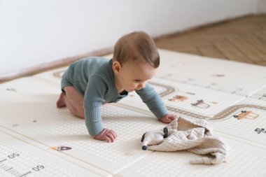 Yumuşak bir oyun hasırının üzerinde karnının üzerine uzanmış duyusal bir oyuncakla oynayan sevimli bir bebek. Bebek, oyuncağı keşfederken odaklanmış ve meraklı, erken öğrenme ve motor beceri geliştirmeyi destekliyor.