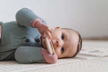 Güzel bir bebeğin tahta bir diş çıkarma oyuncağını tutarken ve çiğnerken yakın plan portresi. Diş çıkarma dönemi, bebek bakımı, erken gelişim ve sağlıklı çocukluk hayatı kavramı.