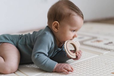 Güzel bir bebeğin tahta bir diş çıkarma oyuncağını tutarken ve çiğnerken yakın plan portresi. Diş çıkarma dönemi, bebek bakımı, erken gelişim ve sağlıklı çocukluk hayatı kavramı.