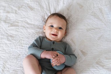 Yumuşak bir battaniyenin üzerinde göbeğin üzerine uzanmış sevimli bir bebek ve renkli bir yüzük oyuncağıyla oynuyor. Erken çocukluk gelişimi, ebeveynlik bakımı, mutlu aile anları ve bebek yaşam tarzı kavramı.