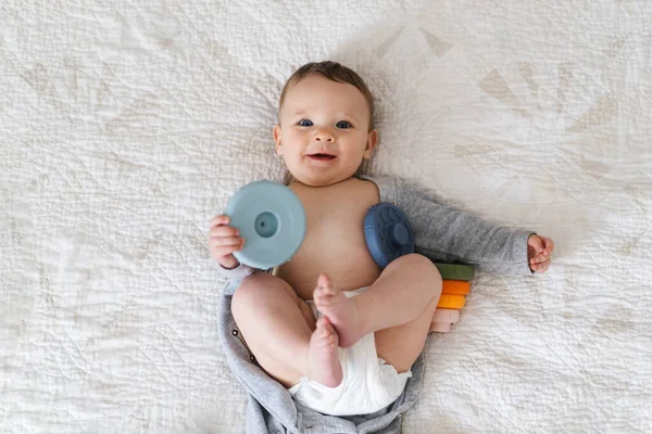 Yumuşak bir battaniyenin üzerinde göbeğin üzerine uzanmış sevimli bir bebek ve renkli bir yüzük oyuncağıyla oynuyor. Erken çocukluk gelişimi, ebeveynlik bakımı, mutlu aile anları ve bebek yaşam tarzı kavramı.