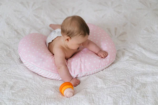 Bebek yumuşak bir yastığa uzanır, renkli bir oyuncağa uzanır. Erken çocukluk gelişimi, ebeveynlik bakımı, mutlu aile anları ve bebek yaşam tarzı kavramı.