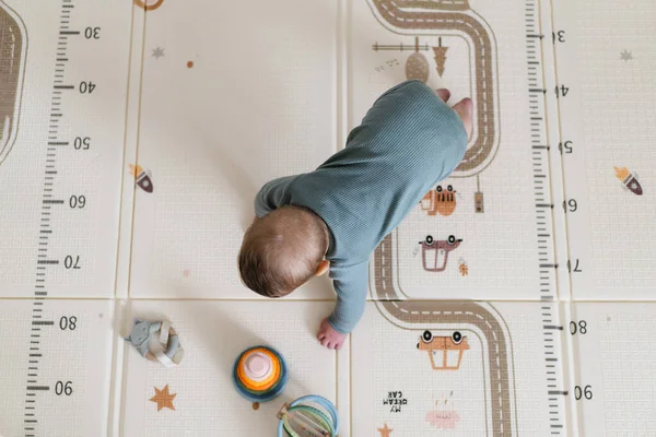 Yumuşak bir oyun hasırının üzerinde karnının üzerine uzanmış duyusal bir oyuncakla oynayan sevimli bir bebek. Bebek, oyuncağı keşfederken odaklanmış ve meraklı, erken öğrenme ve motor beceri geliştirmeyi destekliyor.