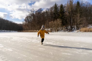 Child having fun in the snow, wearing winter clothing in snowy landscape during daytime. Child with a big smile surrounded by snowy trees and a clear blue sky.