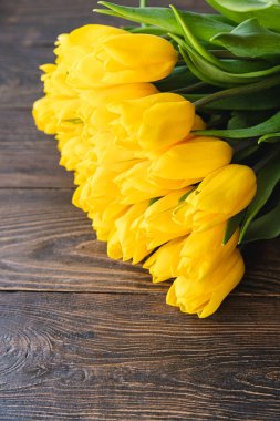 Sarı kurdeleli bir buket sarı lale, ahşap bir arka planda yatıyor. Baharın sembolü. 8 Mart, Anneler Günü, Paskalya veya bahar promosyonları için bayram kartları, selamlar, tasarım için ideal.