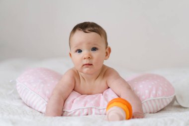 Bebek yumuşak bir yastığa uzanır, renkli bir oyuncağa uzanır. Erken çocukluk gelişimi, ebeveynlik bakımı, mutlu aile anları ve bebek yaşam tarzı kavramı.