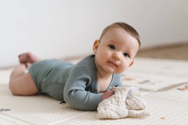 Yumuşak bir oyun hasırının üzerinde karnının üzerine uzanmış duyusal bir oyuncakla oynayan sevimli bir bebek. Bebek, oyuncağı keşfederken odaklanmış ve meraklı, erken öğrenme ve motor beceri geliştirmeyi destekliyor.