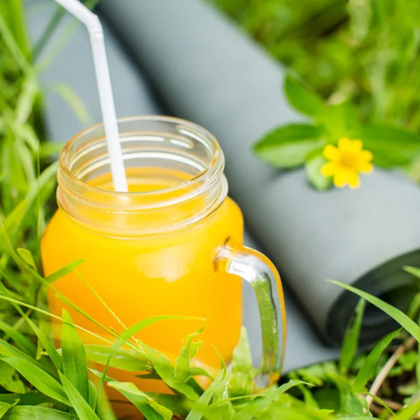 Zumo de naranja fresco y esterilla de yoga en la hierba — Foto de Stock