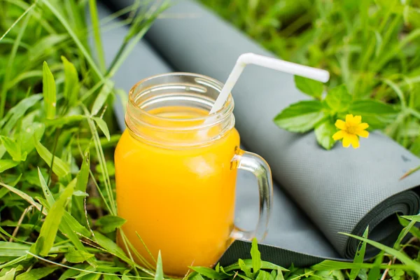 Φρέσκο πορτοκάλι χυμό και γιόγκα χαλάκι στο γρασίδι — Φωτογραφία Αρχείου