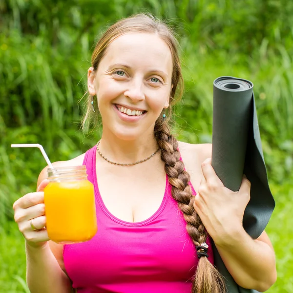 Mujer fitness con esterilla de yoga sosteniendo un vaso de jugo de naranja — Foto de Stock