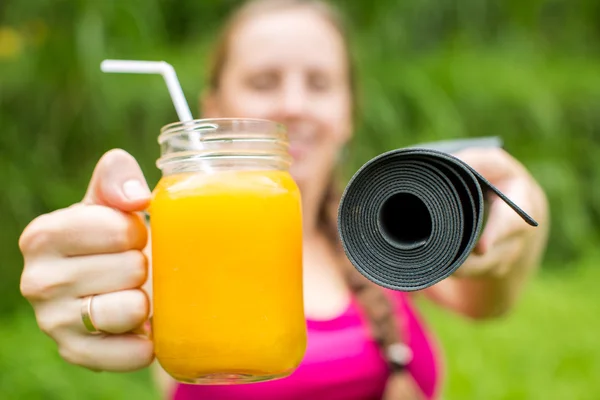 Fitness-Frau mit Yogamatte hält ein Glas Orangensaft in der Hand — Stockfoto