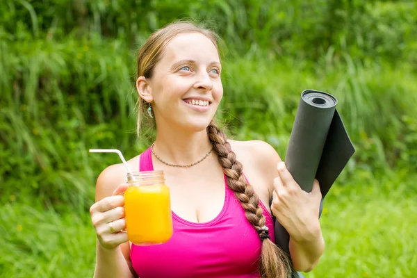 Фитнес-женщина с ковриком для йоги держит стакан апельсинового сока — стоковое фото