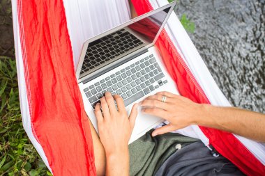 Hamakta yaz tatillerinde dizüstü bilgisayarda çalışan adam.