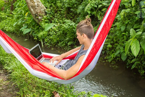 Muž v houpací síti pracují na notebooku během letních prázdnin. — Stock fotografie