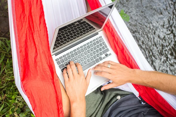 Człowiek w hamak działa na laptopie w okresie wakacyjnym. — Zdjęcie stockowe