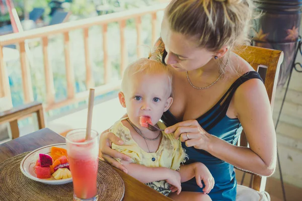 Pretty hipster Mujer alimentar a su hija con desayuno tropical —  Fotos de Stock