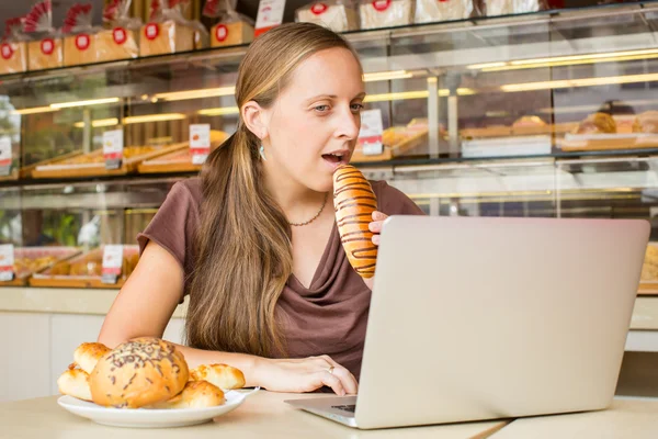 컴퓨터에서 일 하는 젊은 여자를 꽤 하 고 빵을 먹는다. Unheal — 스톡 사진