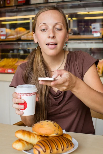 Giovane donna in chat telefono cellulare con una torta nel caffè — Foto Stock