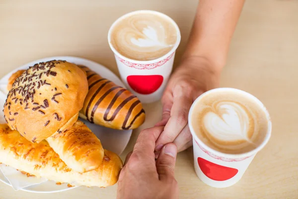 Cuatro manos envueltas alrededor de una taza de café con dibujo del corazón — Foto de Stock