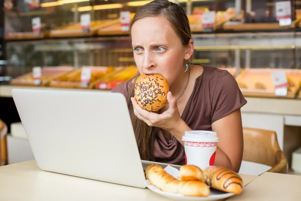 Uma jovem bonita a trabalhar no computador e a comer pão. Não cicatrizar — Fotografia de Stock